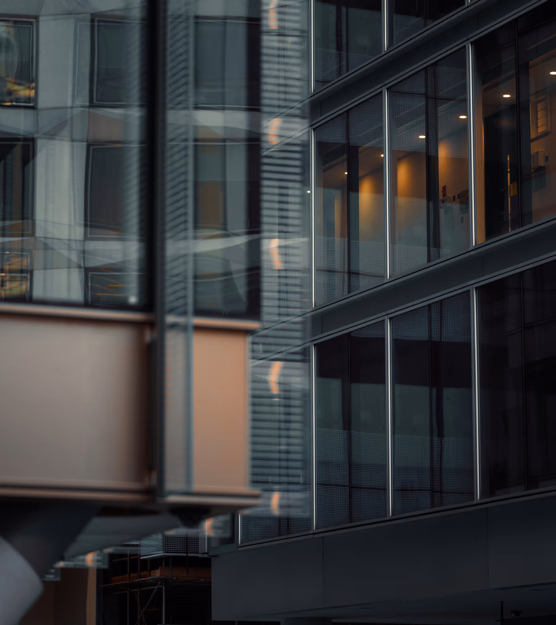 Close-up of modern office building windows reflecting nearby structures with some interior lights visible.